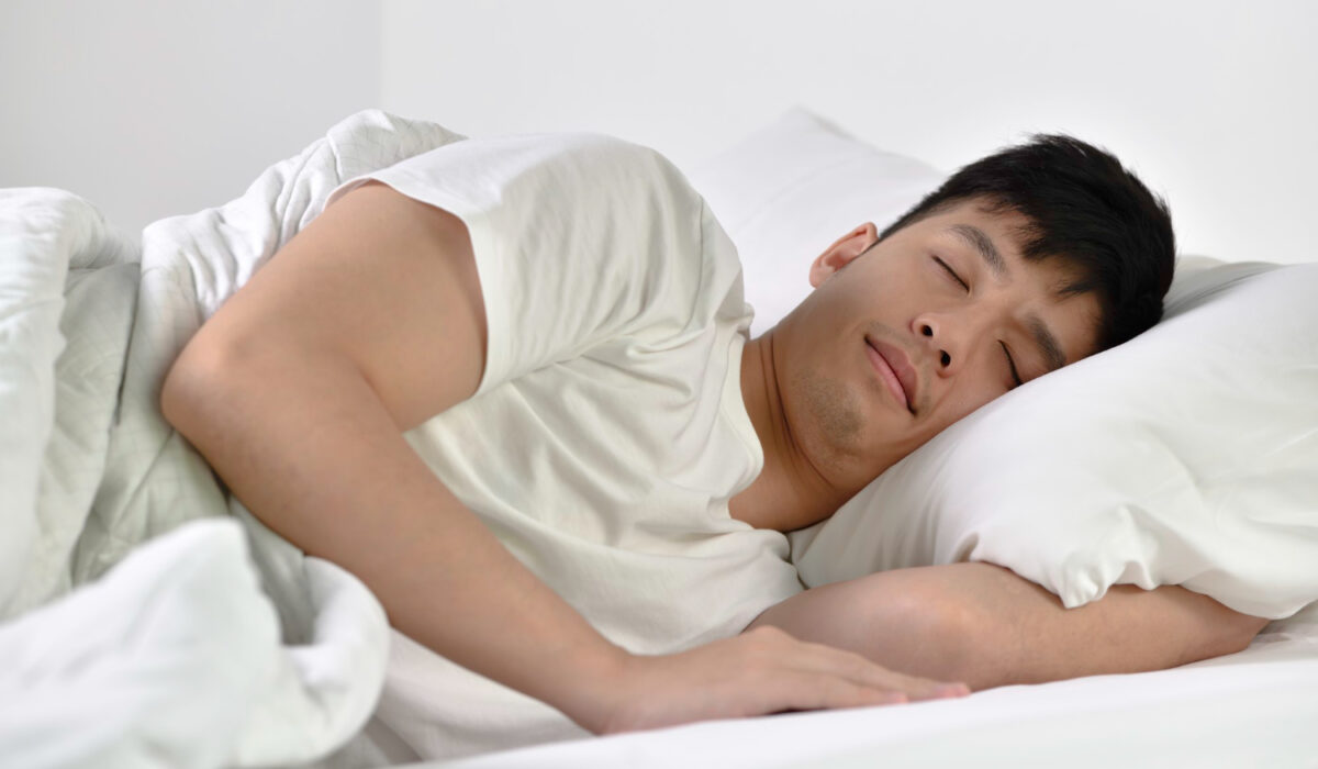 Man sleeping on his side in white bed with pillows and a blanket.