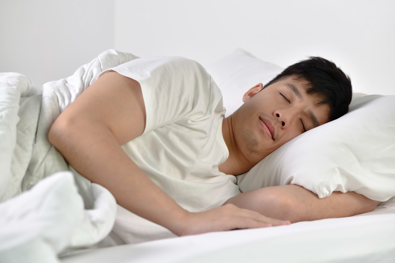 Man sleeping on his side in white bed with pillows and a blanket.